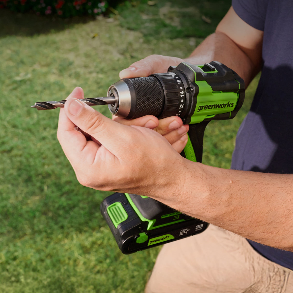 Person holding a Greenworks drill with a drill bit outdoors on grass