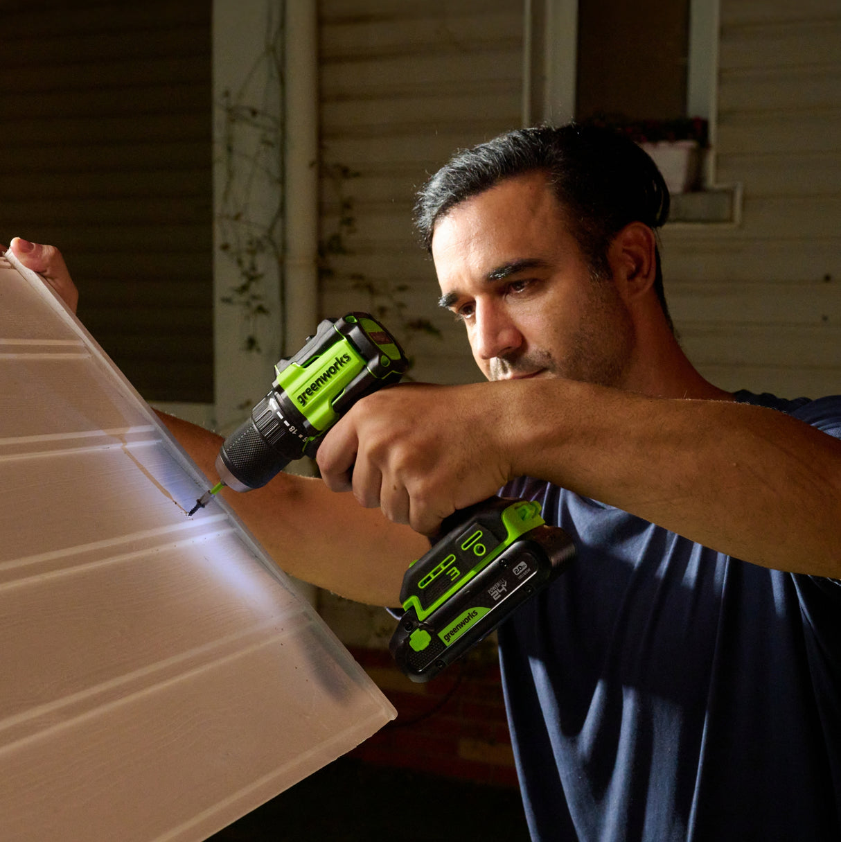 Man using a green and black power drill on a wooden surface