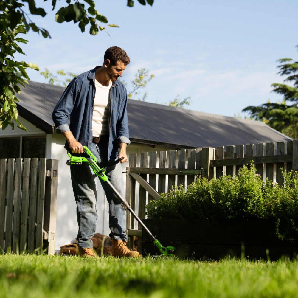 Man using a lawn mower in a garden with a wooden shed in the background