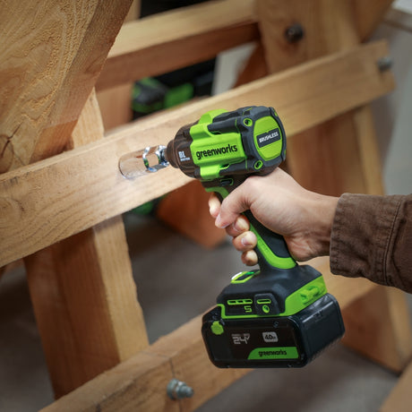 Person using a greenworks cordless drill on wooden furniture.