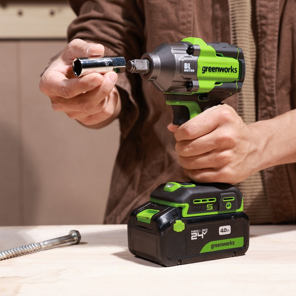 Person using a Greenworks cordless drill with a battery pack on a wooden surface.