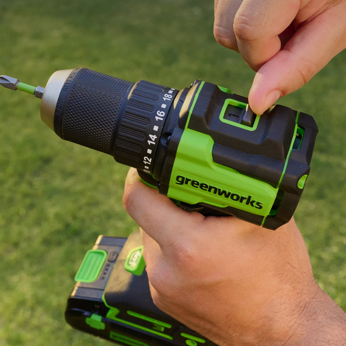 Hand holding a Greenworks drill with a green background
