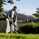 Man using a lawn mower in a garden with a wooden shed in the background
